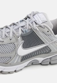 Grå träningsskor med en meshuvud, texturerade grå detaljer, framträdande vitt swoosh-logotyp, vadderad krage och dämpad yttersole.