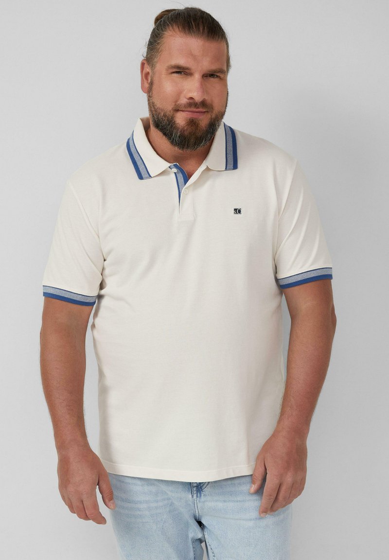 Crème polo shirt met blauwe gestreepte kraag en mouwaccenten. Beschikt over een klein logo op de borst. Gecombineerd met lichtblauwe jeans.