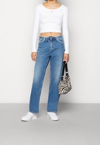 Vit långärmad crop top med liten röd logotyp, matchad med ljusblå vida jeans. Svart och vit zebra-mönstrad väska och vita sneakers.