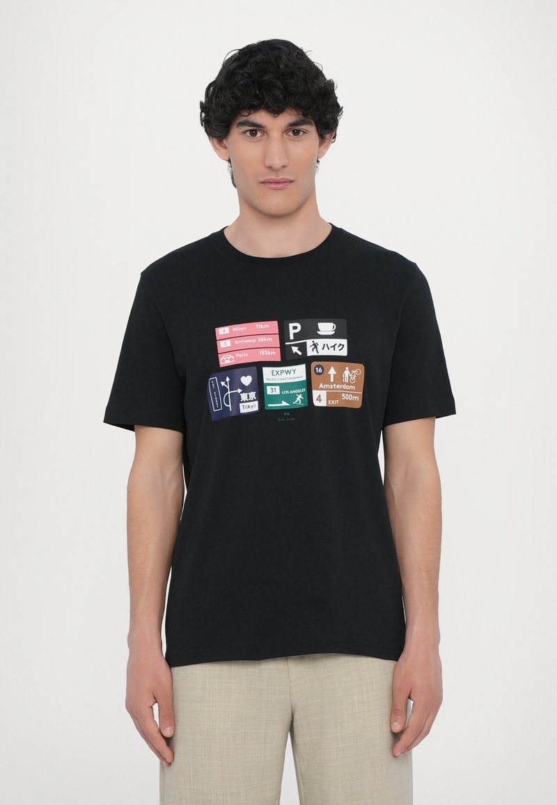 T-shirt en coton noir avec un graphisme imprimé représentant des panneaux de voyage dans diverses couleurs et langues, manches courtes et coupe standard.