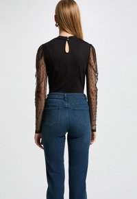 Top nero con maniche trasparenti a pois e schiena a fessura, abbinato a jeans blu a vita alta con tasche posteriori e design aderente.