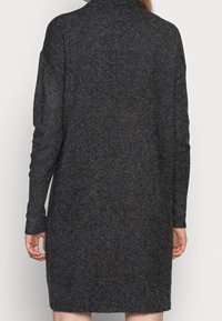 Robe pull en tricot gris foncé avec un col haut, des manches longues et une coupe fluide, présentant un tissu texturé et une couleur uniforme.