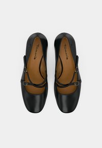 Μαύρα δερμάτινα παπούτσια τύπου φλατ με στρογγυλή μύτη, που διαθέτουν δύο διασταυρούμενες λουρίδες, λεπτομέρεια με πόρπη και λεία υφή. Ορατός καφέ εσωτερικός πάτος.