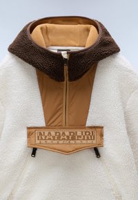 Lunefuldt hvidt fleece-pullover med en brun, Sherpa-foret krave. Har et brunt brystpanel med logo og lynlås lukning. Blød tekstur overalt.