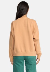 Lichtbruine sweatshirt met een relaxte fit, verlaagde schoudernaden, ribgebreide manchetten en zoom. Gecombineerd met groene broek.