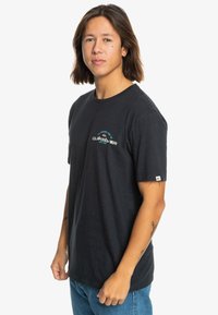 Černé bavlněné tričko s kulatým výstřihem, krátkými rukávy a modro-bílým logem Quiksilver na hrudi. Nosené s modrými džíny.