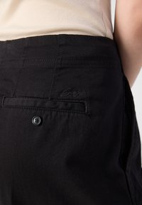 Sorte denim-bukser med baklomme som har brodert logo og knappelukking. Jevn tekstur, standard passform, og enkel design.