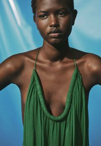 Robe verte sans manches avec un décolleté en V profond et une texture drapée. Fabriquée en tissu léger avec des accents plissés.