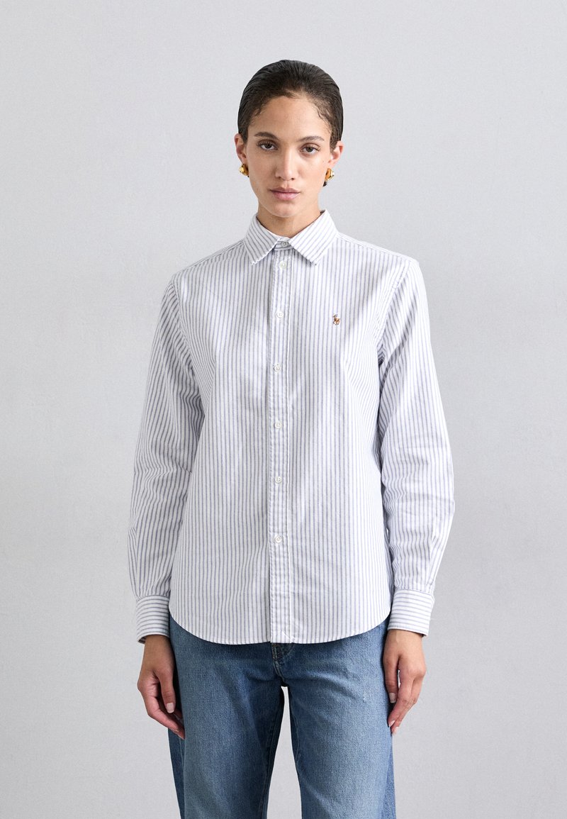 Chemise à rayures bleues et blanches avec col, dotée de manches longues et d'un petit logo sur la poitrine. Tissu en coton, texture lisse.