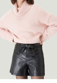 Helles rosa, flauschiges Strickoberteil mit einem gerippten Rollkragen, kombiniert mit hochgeschnittenen schwarzen Leder-Shorts mit einem Bindegürtel und glattem Finish.