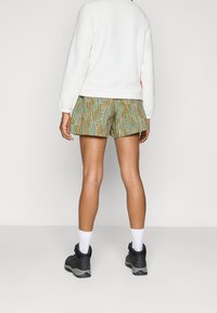 Los pantalones cortos presentan un patrón geométrico multicolor con acentos en verde, naranja y azul, confeccionados con un material ligero. Llevados con un sudadera blanca.