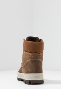 Hnědé semišové kotníkové boty s hnědým vrškem, bílým prošitím a gumovou podrážkou s texturovaným gripem. Pohled ze zadu, ukazující měkkou podšívku.