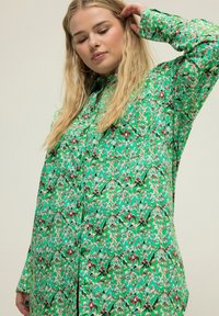 Camicia verde a maniche lunghe con bottoni, caratterizzata da intricati motivi floreali e astratti, con colletto e vestibilità comoda.