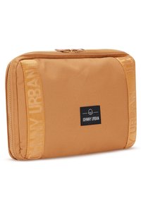 Tan rektangulär dragkedjepåse med "Johnny Urban"-etikett och matchande varumärkesremsor på vardera sidan, vinklad på en vit bakgrund.