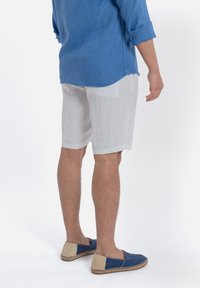 Linnen blauwe shirt met opgerolde mouwen, witte linnen shorts en twee-tint espadrilles met blauwe en beige accenten. Neutrale achtergrond.