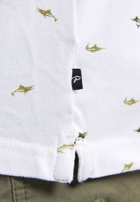 Bílá polo košile s zelenými rybími vzory, texturovaná tkanina, postranní rozparky a námořnická etiketa s bílým logem "P" na lemu.