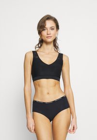 Bralette nera senza cuciture con dettagli in pizzo su spalline larghe, abbinata a mutandine nere a vita alta con una cintura logata. Texture liscia.