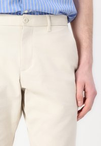 Beige bomuldsbukser med sidelommer, skræddersyet pasform og knaplukning. Glat tekstur med minimale syninger.