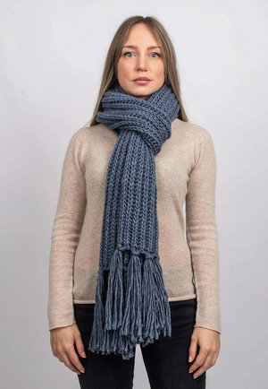 Écharpe bleu chunky en tricot avec des extrémités à franges, fabriquée en laine douce, drapée autour du cou d'une personne portant un pull léger beige.