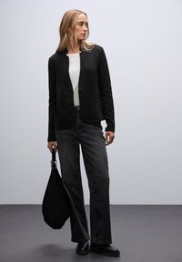 Zwarte textuur jasje met een ronde kraag, enkele knop, gecombineerd met een witte top en donkere, wijde jeans, met een zwarte tote bag.