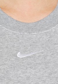 Grå sweatshirt tillverkad av bomullsmix med ribbat krage. Har en vit broderad Nike swoosh-logotyp på bröstet.