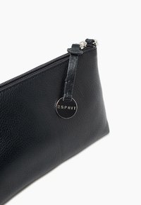 Pochette en cuir noir avec finition texturée, fermeture éclair et languette en cuir. Présente un logo métallique rond en accent.