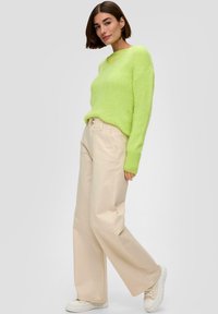 Limonkowy, teksturowany sweter z dekoltem w serek, w połączeniu z kremowymi spodniami o szerokich nogawkach i białymi trampkami z grubymi podeszwami.