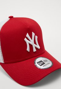 Casquette de baseball rouge avec un dos en mesh blanc, arborant un logo "NY" brodé en blanc sur le devant et une étiquette circulaire ajustable sur le bord.