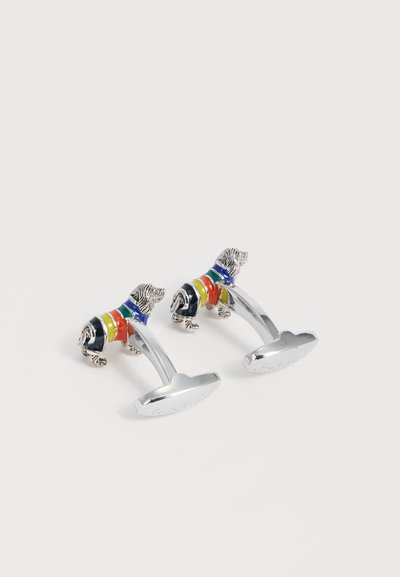 Boutons de manchette en argent en forme de petits chiens portant des pulls rayés en bleu, vert, jaune et rouge, placés sur un fond blanc.