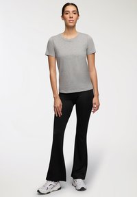 Szary t-shirt z krótkim rękawem w połączeniu z czarnymi spodniami w dzwony. Spodnie mają gładką teksturę, a model ma na sobie białe buty sportowe.