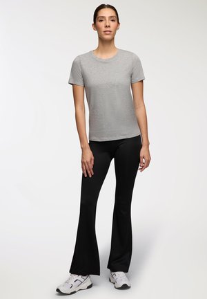 T-shirt grigio a maniche corte abbinato a pantaloni neri a campana. I pantaloni hanno una texture liscia e il modello indossa scarpe da ginnastica bianche.