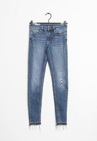 Vaqueros skinny en denim azul medio con ligero desgaste y dobladillo deshilachado. Presentan bolsillos frontales y una cintura estándar con pasadores para cinturón.
