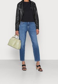 Svart läder bikerjacka, svart t-shirt, ljusblå högmidjade jeans, grön handväska, svarta klacksandaler, minimalistisk design.