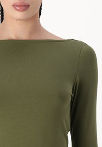 Olivgrön långärmad topp i mjukt, elastiskt tyg, med en vid halsringning och rena sömmar längs kanterna.