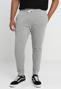 Pantalones de chándal grises hechos de una tela suave, con una cinturilla elástica con cordón, piernas ajustadas y puños acanalados, combinados con zapatillas negras.
