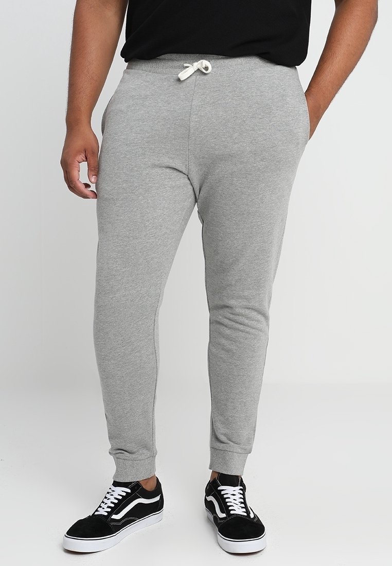 Pantalones de chándal grises hechos de una tela suave, con una cinturilla elástica con cordón, piernas ajustadas y puños acanalados, combinados con zapatillas negras.