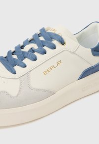Hvite lær sneakers med blå snøring og detaljer, med et grått gammmelpanel og gull "REPLAY" merke på siden.