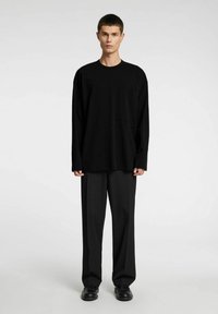 Svart langermet t-skjorte med brystlomme, rund hals, løs passform, kombinert med svarte vide bukser og svarte sko. Minimalistisk design.