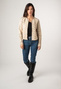 Giacca cropped beige con design a righe verticali, chiusura con zip e maniche lunghe. Abbinata a jeans blu e stivali neri al ginocchio.