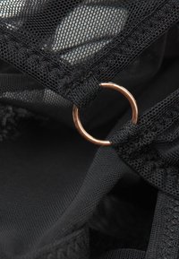 Närbild av svart mesh-tyg med en liten guldring genomsydd i materialets kant.