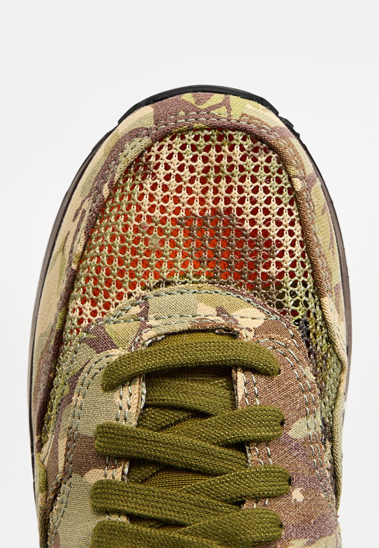 Zapatilla de camuflaje con parte superior de malla, cordones en color verde olivo y suela de goma. Destacada por sus patrones texturizados y diseño transpirable.