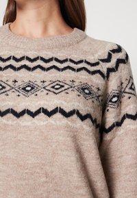 Maglione beige a maglia con collo rotondo, caratterizzato da motivi geometrici neri, comprese zig-zag e diamanti, nella zona del petto.