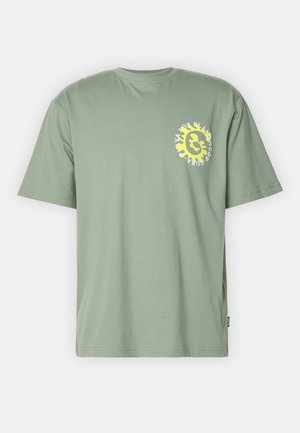 T-shirt en coton vert à manches courtes, avec un graphisme circulaire jaune et du texte sur le côté gauche de la poitrine. Design simple à col rond.