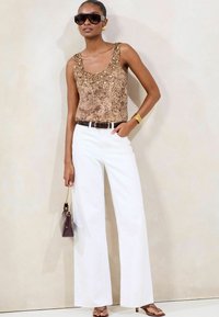 Brown patterned sleeveless top with embellishments, paired with white wide-leg jeans, black belt, and a small dark handbag.