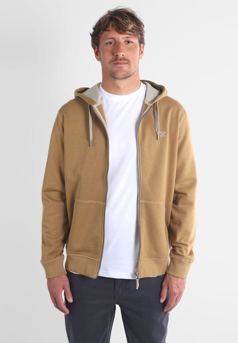 Haut à capuche zippé beige avec un intérieur gris clair. Doté de poches avant, de cordons de serrage et de bords côtelés aux manches et à l'ourlet.