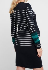 Těhotenské šaty s dlouhým rukávem v námořnické modré a bílé pruhy s tyrkysovými akcenty na rukávech, žebrované manžety a přiléhavý silueta.