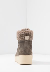 Bottine en daim marron avec une bordure en tricot peluche beige, bout rond et semelle plateforme surélevée. Dispose d'une boucle arrière pour un enfilage facile.