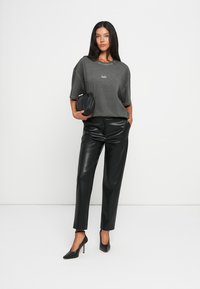 T-shirt cinza oversize com decote redondo e mangas curtas, combinado com calças pretas de couro sintético e saltos altos pretos.