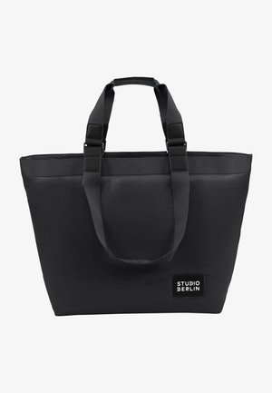 Schwarze Tragetasche aus strapazierfähigem Stoff. Verfügt über zwei obere Griffe, eine rechteckige Form und ein Logo-Patch mit "STUDIO BERLIN" in weißem Text.