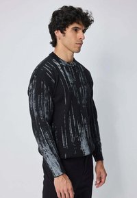 Pull noir avec un motif texturé et des stries grises, encolure ronde et manches longues. Coupe décontractée avec des poignets côtelés.
